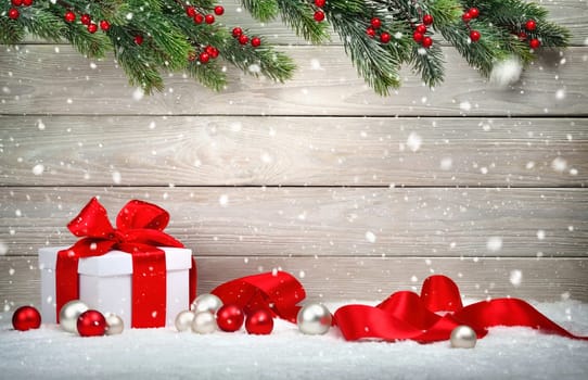 Christmas wood background with a white gift box,red bow and ribbon,baubles,fir branches and snow