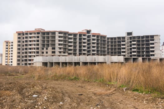Abandoned construction of multi-storey residential complex, overgrown with weeds
