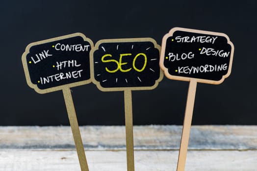 Concept message SEO as Search Engine Optimization written with chalk on wooden mini blackboard labels, defocused chalkboard and wood table in background