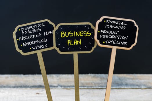 Concept message BUSINESS PLAN written with chalk on wooden mini blackboard labels, defocused chalkboard and wood table in background