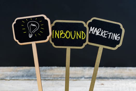 Concept message INBOUND MARKETING and light bulb as symbol for idea written with chalk on wooden mini blackboard labels, defocused chalkboard and wood table in background