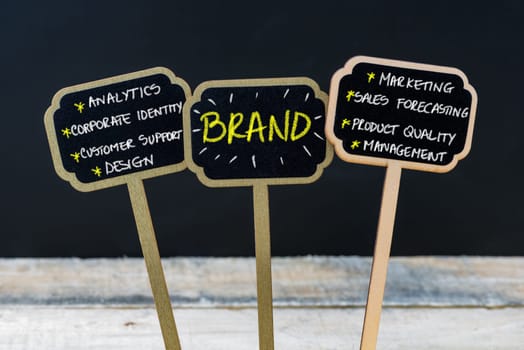 Concept message BRAND written with chalk on wooden mini blackboard labels, defocused chalkboard and wood table in background