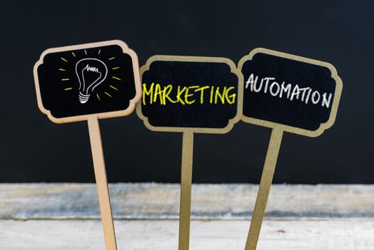 Concept message MARKETING AUTOMATION and light bulb as symbol for idea written with chalk on wooden mini blackboard labels, defocused chalkboard and wood table in background