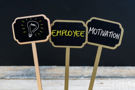 Concept message EMPLOYEE MOTIVATION and light bulb as symbol for idea written with chalk on wooden mini blackboard labels, defocused chalkboard and wood table in background