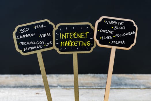 Concept message INTERNET MARKETING written with chalk on wooden mini blackboard labels, defocused chalkboard and wood table in background