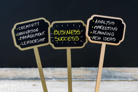 Concept message BUSINESS SUCCESS written with chalk on wooden mini blackboard labels, defocused chalkboard and wood table in background