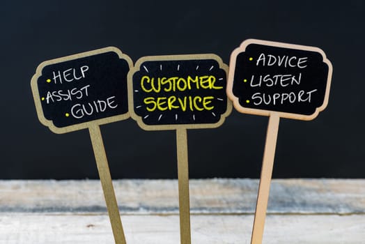 Concept message CUSTOMER SERVICE written with chalk on wooden mini blackboard labels, defocused chalkboard and wood table in background