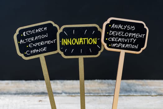 Concept message INNOVATION written with chalk on wooden mini blackboard labels, defocused chalkboard and wood table in background