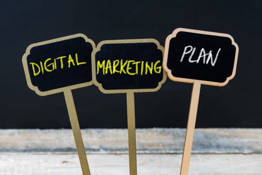 Concept message DIGITAL MARKETING PLAN written with chalk on wooden mini blackboard labels, defocused chalkboard and wood table in background