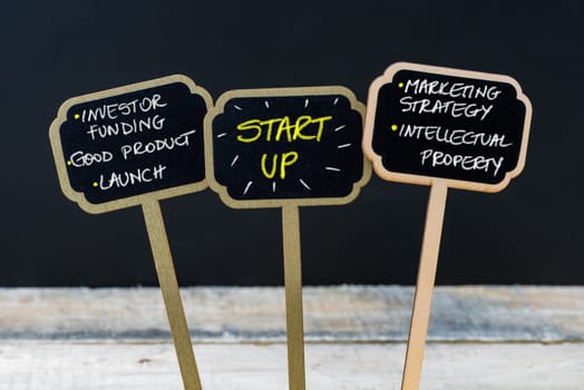 Concept message START UP written with chalk on wooden mini blackboard labels, defocused chalkboard and wood table in background