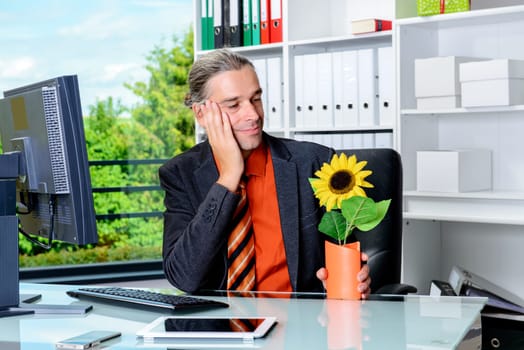 young business man at his desk looking at his sunflower