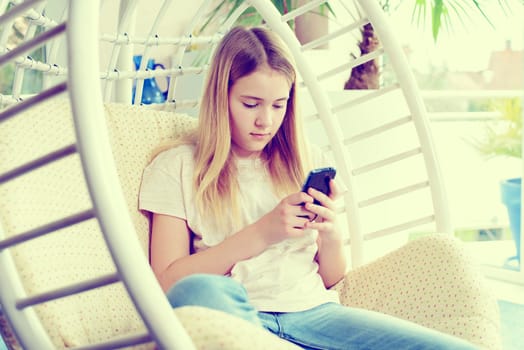 blond girl with phone sitting in chair at home