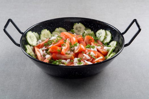A bunch of sliced red tomatoes with cucumber and onion in a round metal bowl