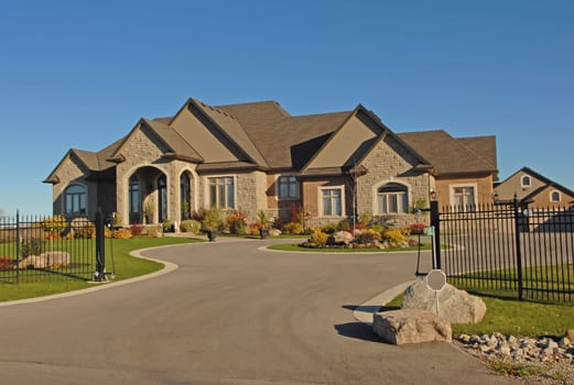 The front few of a new large mansion on a gig lot and driveway with a.iron black fence around in the fall..
