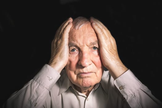 Portrait of an elderly man with face closed by hands on black