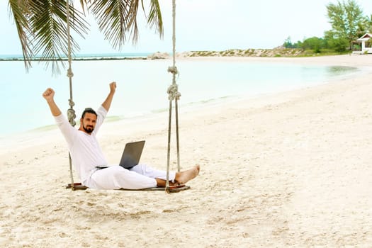 Businessman wearing white freelance sitting on beach swing with laptop