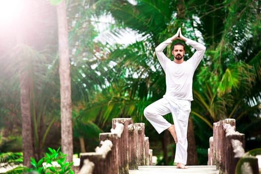 Man wearing white doing yoga in tropic jungle