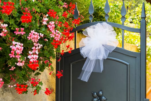 View of a bridal bow put on an iron gate with colorful flowers on the left