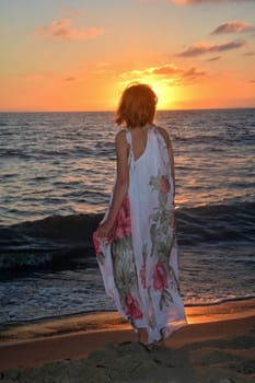 Girl in a long dress stands on the sea beach at sunset,with a view to the sun,head covers the sun