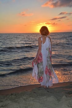 Girl in a long dress stands on the sea beach at sunset,with a view to the sun,head covers the sun