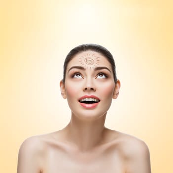 Close-up of beautiful young woman looking up on sun drawing on her forehead. Isolated over beige background. Copy space. Square composition.