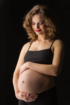 Attractive young woman hugging her pregnant belly over black background