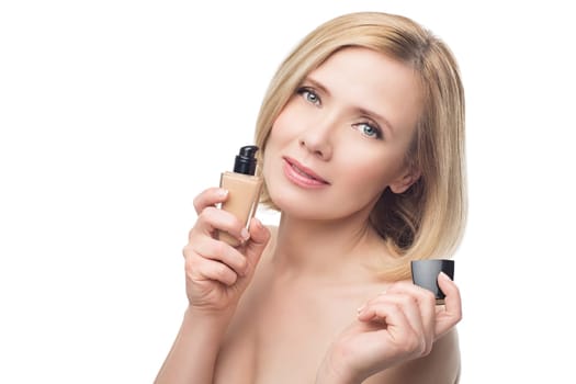 Beautiful middle aged woman with smooth skin and short blond hair holding face foundation cream. Beauty shot. Isolated over white background. Copy space.