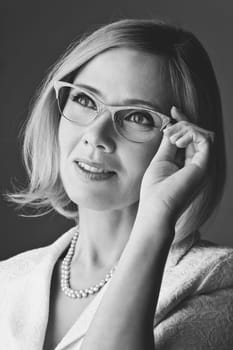 Closeup of elderly business woman in glasses. Happy smiling expression. Over grey background. Monochrome.