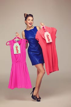 Beautiful happy woman holding  two dresses on hangers. Price tags. Over grey background. Copy space.