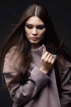 Beautiful young girl with bright makeup wearing coat over dark background