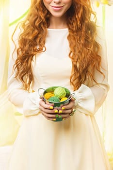 Closeup of beautiful young woman in dress holding small aluminium basket with yellow and green wool balls.