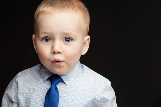 Handsome funny little boy wearing shirt and blue tie with expression of surprise on face. True emotions. Studio shot. Horizontal. Copy space.