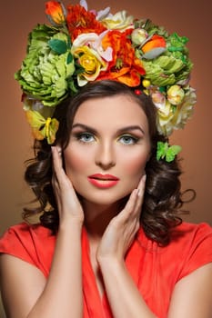 Beautiful young woman with bright colorful make up and flowers on her head. Isolated over brown background