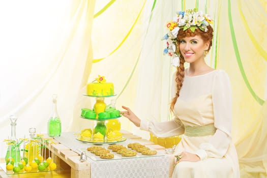 Beautiful young bride in yellow dress with red braided hair sitting near dessert table. Copy space.