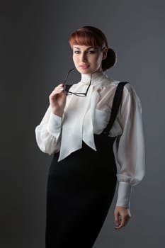 Beautiful young woman in fashionable glasses wearing blouse and skirt. Over grey background. Copy space. Vertical.