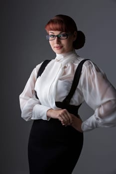 Beautiful young woman in fashionable glasses wearing blouse and skirt. Over grey background. Copy space. Vertical.