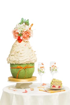 Table with stylish wedding cake and two champagne glasses decorated with flowers standing on it. Isolated over white background