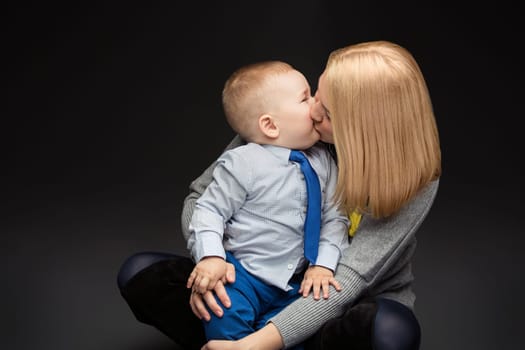 Yong woman kissing child over dark background. Mother and son. Studio shot, Copy space.
