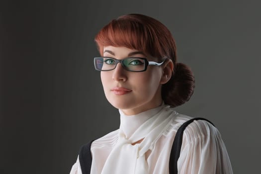 Closeup of beautiful young woman in white blouse and glasses over grey background