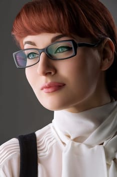 Closeup of beautiful young woman in white blouse and glasses over grey background