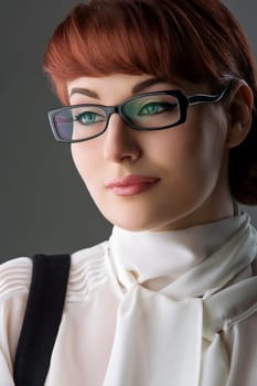Closeup of beautiful young woman in white blouse and glasses over grey background