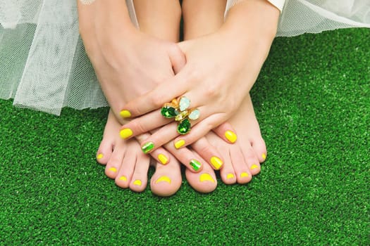 Closeup of woman toes and fingers with yellow, green nail polish.