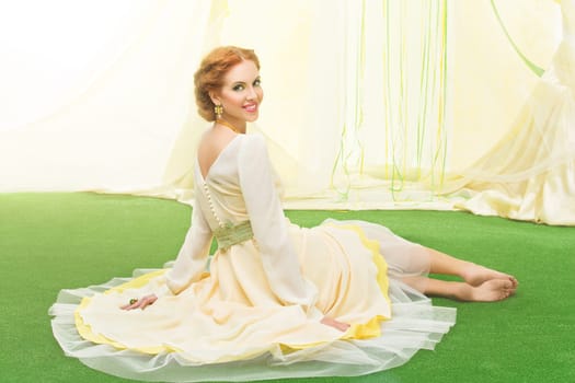 Beautiful young woman in yellow dress sitting on lawn