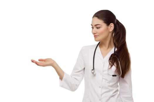 Portrait of beautiful young smiling woman dressed as doctor showing something with hand. Isolated over white background. Copy space.
