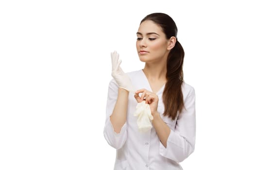 Beautiful young doctor woman in medical white coat putting on rubber gloves. Isolated over white background. Copy space.