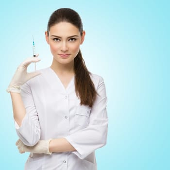 Beautiful young doctor in medical robe holding syringe with liquid. Isolated over blue background