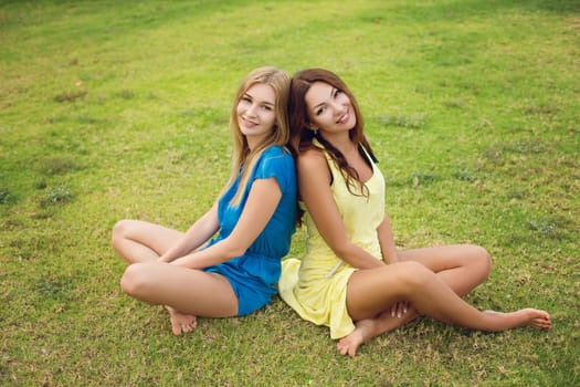 Two beautiful women sitting on grass. Outdoor shot.
