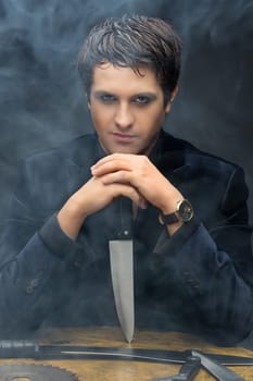Mysterious handsome guy with knives in smoke over black background