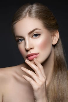 Beautiful young woman with blond hair and nude pink lips touching face. Over black background. Closeup beauty shot.