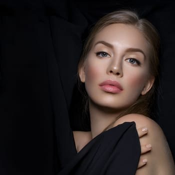 Beautiful young woman with blond hair and makeup covered with piece of black fabric. Beauty shot. Over black background. Copy space. Square composition.